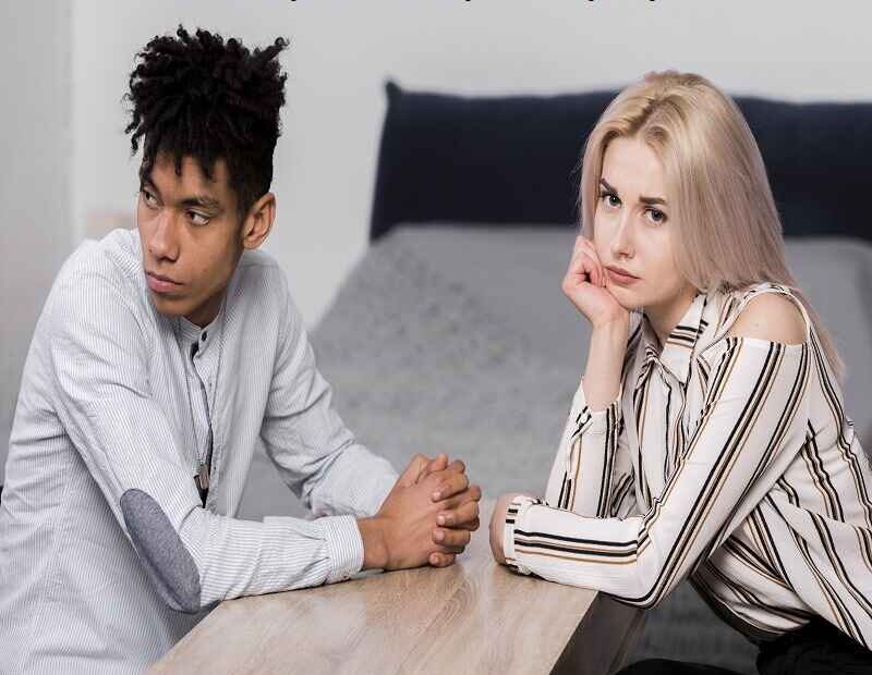 Sad couple sitting across from each other, looking away with serious expressions, symbolizing the concept of 'a true relationship is two imperfect people refusing to give up.