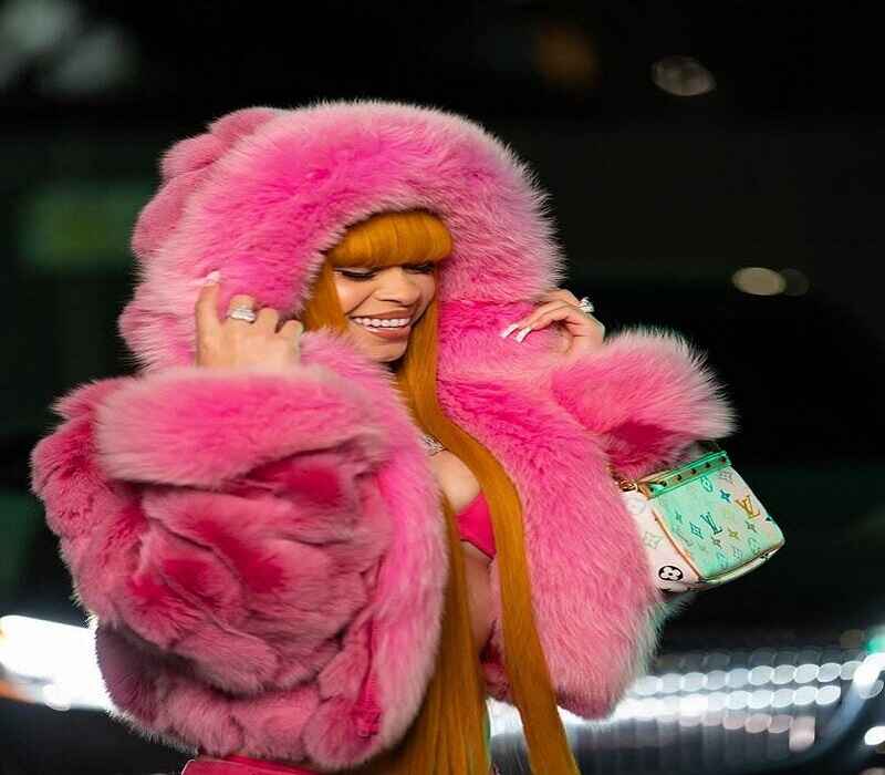 Ice Spice wearing a vibrant pink fur coat, smiling confidently, and showcasing her unique fashion style.