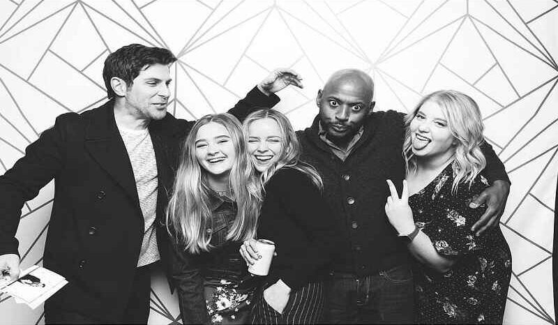 Lizzy Greene is posing with four friends in a black-and-white photo. They are smiling, making funny faces, and appear to be enjoying a lighthearted moment together. The group is standing close, showing camaraderie and a fun atmosphere.