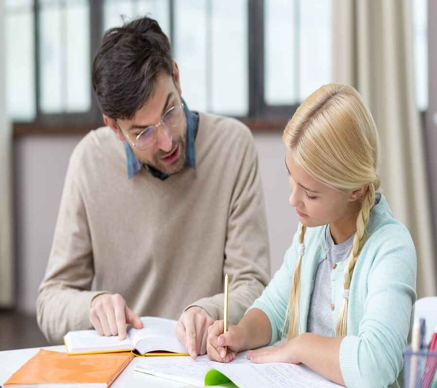 A male tutor discussing homework with a young female student at a table.